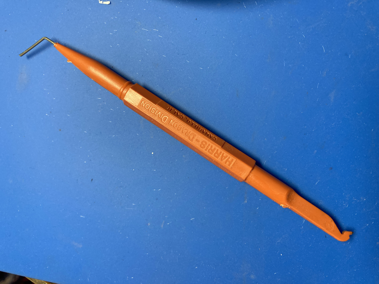 Photo of mystery tool, which is bright orange and about the size of a pencil. Has a wire poking from one end, and a slight hook at the other. 