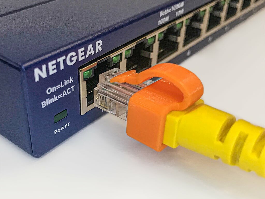 A picture of an 3D printed orange RJ45 clip to secure/repair/fix a broken  tab on an ethernet cable.
The clip is already placed on an ethernet with a missing tab, and ready to be connected to a blue box Netgear switch.